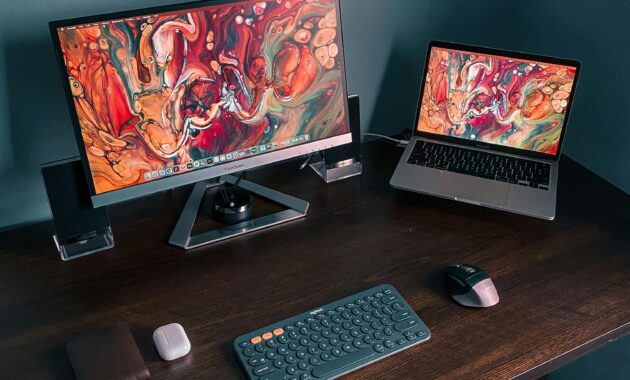 A modern home office with dual screens displaying vibrant abstract art, ideal for tech enthusiasts.